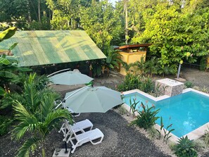 Ein Poolbereich mit Liegestühlen und Sonnenschirmen, umgeben von tropischen Pflanzen und einer überdachten Struktur.