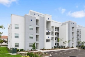 A modern multi-story residential building with balconies, a parking lot, and landscaped areas. - Cozy 3BR in Storey Lake 10 Min From Disney! (Kissimmee)