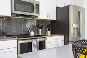 Een moderne keuken met witte kastjes, een RVS magnetron, een waterkoker en een koelkast.