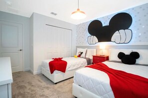 Een hotelkamer met twee bedden, een Mickey Mouse decoratie aan de muur, en een rode plaid op een van de bedden.