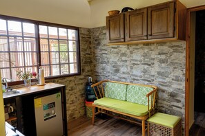 A compact kitchen with a built-in fridge, a bench with a cushion, a window with a view, and a stone wall. - Your retreat for relaxation in Boquete (Panamá)