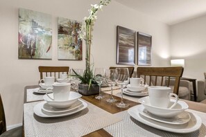A dining table set with white plates, cups, and glasses, surrounded by chairs. - 3BR Lucaya Village Home, Sleeps 8 (Kissimmee)