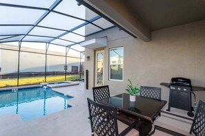 A covered outdoor area with a pool, a table with chairs, and a grill. - Storey Lake 5BR Home Resort + Pool (Kissimmee)