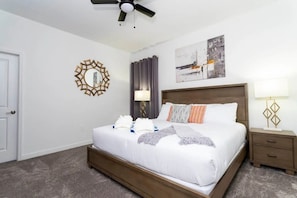 A hotel room with a large bed, a ceiling fan, a nightstand with a lamp, a wall mirror, and a painting. - Storey Lake 5BR Home Resort + Pool (Kissimmee)