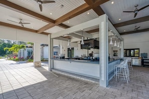 An outdoor bar area with a counter, ceiling fans, and hanging pendant lights. - Storey Lake 5BR Home Resort + Pool (Kissimmee)