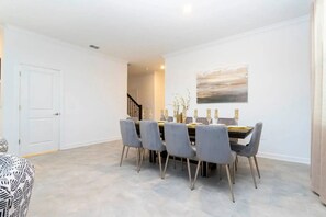 A dining area with a table set for six, six grey chairs, and a modern painting on the wall. - Storey Lake 5BR Home Resort + Pool (Kissimmee)