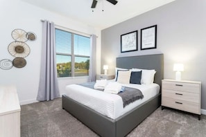 A modern bedroom with a large bed, two bedside tables, a view of the outdoors, and decorative wall art. - Storey Lake 5BR Home Resort + Pool (Kissimmee)