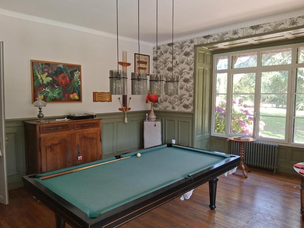 A pool table in a room with a wooden cabinet, a painting, and a window with a view of greenery.