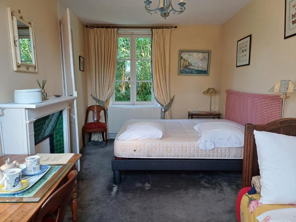 Ein Schlafzimmer mit einem Bett, einem Sessel, einem Tisch mit Teekanne, einer Lampe und einem Fenster mit Vorhängen.