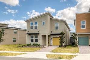 A two-story residential building with a flat roof, a garage, and a small front yard with grass and shrubs. - Luxury 6BR Home at Storey Lake Near Disney (Kissimmee)
