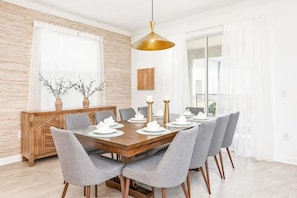 A dining area with a wooden table set for six, grey upholstered chairs, a gold pendant light, and a decorative wall panel. - Luxury 6BR Home at Storey Lake Near Disney (Kissimmee)