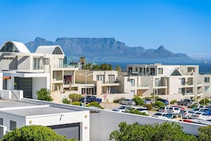 A modern hotel with multiple balconies, a parking lot, and a view of the ocean and mountains. - Azure 119 (Cape Town)