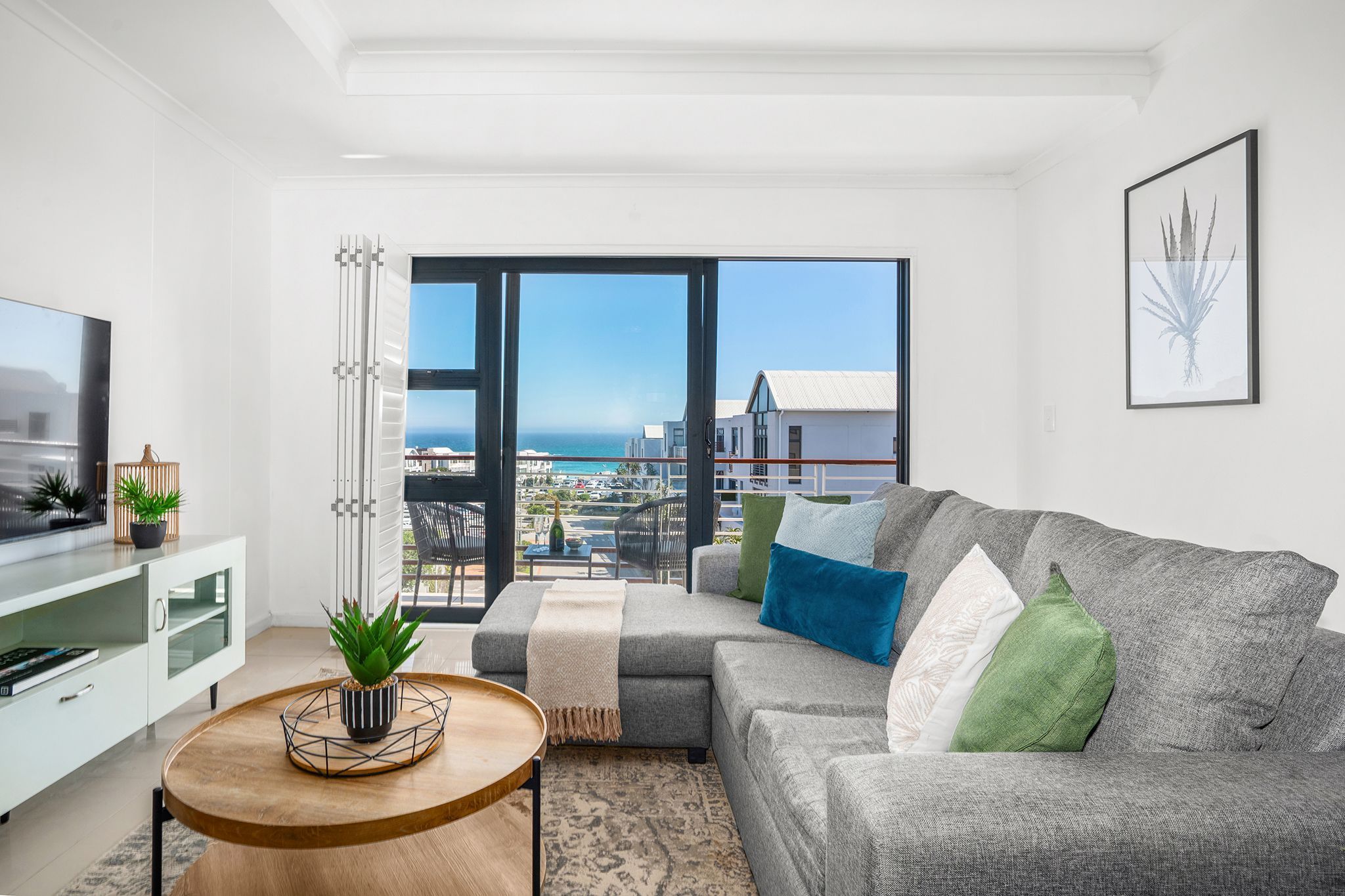 A modern living room with a grey sofa, a round wooden coffee table, and a television on a white cabinet.