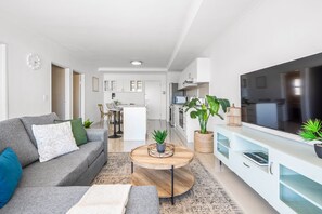 A modern living room with a grey sofa, a wooden coffee table, and a TV on a white cabinet. - Azure 119 (Cape Town)