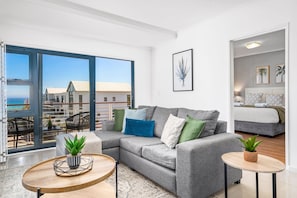 A modern living room with a grey sofa, a round wooden coffee table, and a view of the sea through large windows. - Azure 119 (Cape Town)