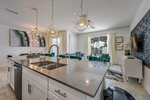 Une cuisine moderne dotée d’un îlot central, d’appareils électroménagers en acier inoxydable et de luminaires suspendus.