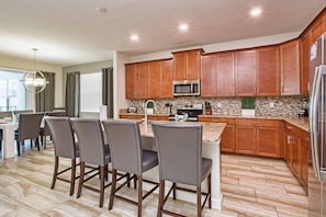 A modern kitchen with wooden cabinets, a stainless steel refrigerator, and a granite countertop. - 6BR Home Private Pool 10 Min to Disney! (Kissimmee)