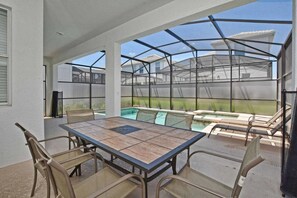 A covered patio with a pool, outdoor seating, and a table. - 6BR Home Private Pool 10 Min to Disney! (Kissimmee)