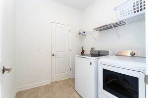 A laundry room with a white door, two washing machines, and a drying rack. - 5BR Villa w/ Pool & Disney Themes (Kissimmee)
