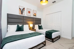 A hotel room with two beds, a grey headboard, a white door, and a wall with three framed pictures. - 5BR Villa w/ Pool & Disney Themes (Kissimmee)