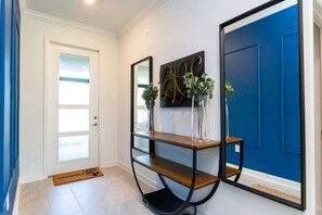 Un couloir avec une porte blanche, une porte bleue, une console en bois ornée de deux vases et un miroir à cadre noir.