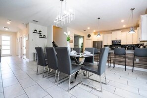 A modern kitchen with stainless steel appliances, a dining area with a glass table and black chairs, and a chandelier. - Luxury 6BR w/ Pool + Game Room Near Disney (Kissimmee)