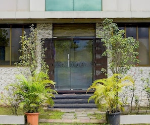 A building entrance with a glass door, steps leading up to it, and potted plants on either side. - Classic Hotel Shivneri (Vasai)