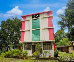 A hotel with a sign reading 'HOTEL' and a company-serviced symbol. It features a multi-story structure with a mix of red and white walls and green-tinted windows. - Classic Hotel Shivneri (Vasai)