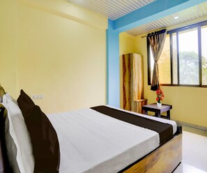 A hotel room with a bed, a window with curtains, a small table with a vase, and a wardrobe. - Classic Hotel Shivneri (Vasai)