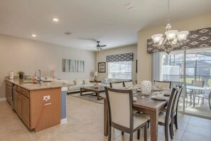 A spacious living area with a kitchen, dining table, and a large window offering a view of the outdoors. - Family Retreat: 4BR Townhome w/ Pool (Kissimmee)
