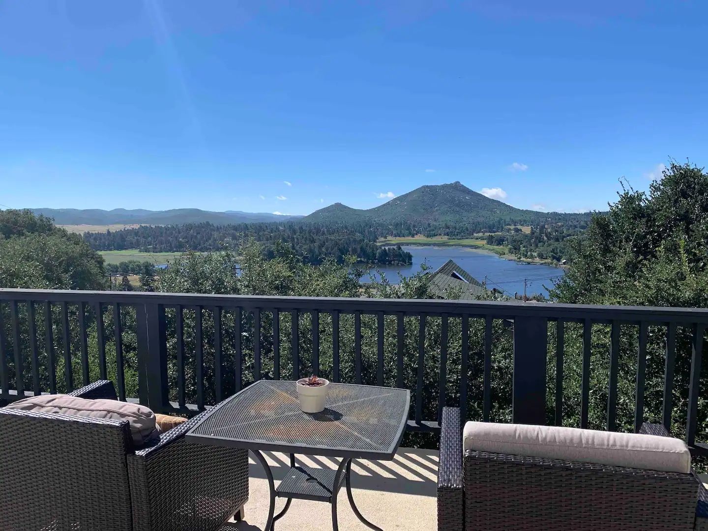 A balcony with wicker furniture, a table, and a view of a lake and mountains.