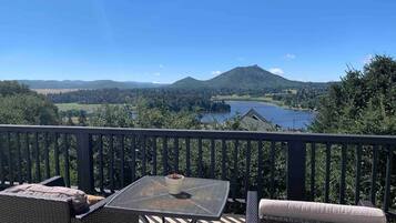 A balcony with wicker furniture, a table, and a view of a lake and mountains.