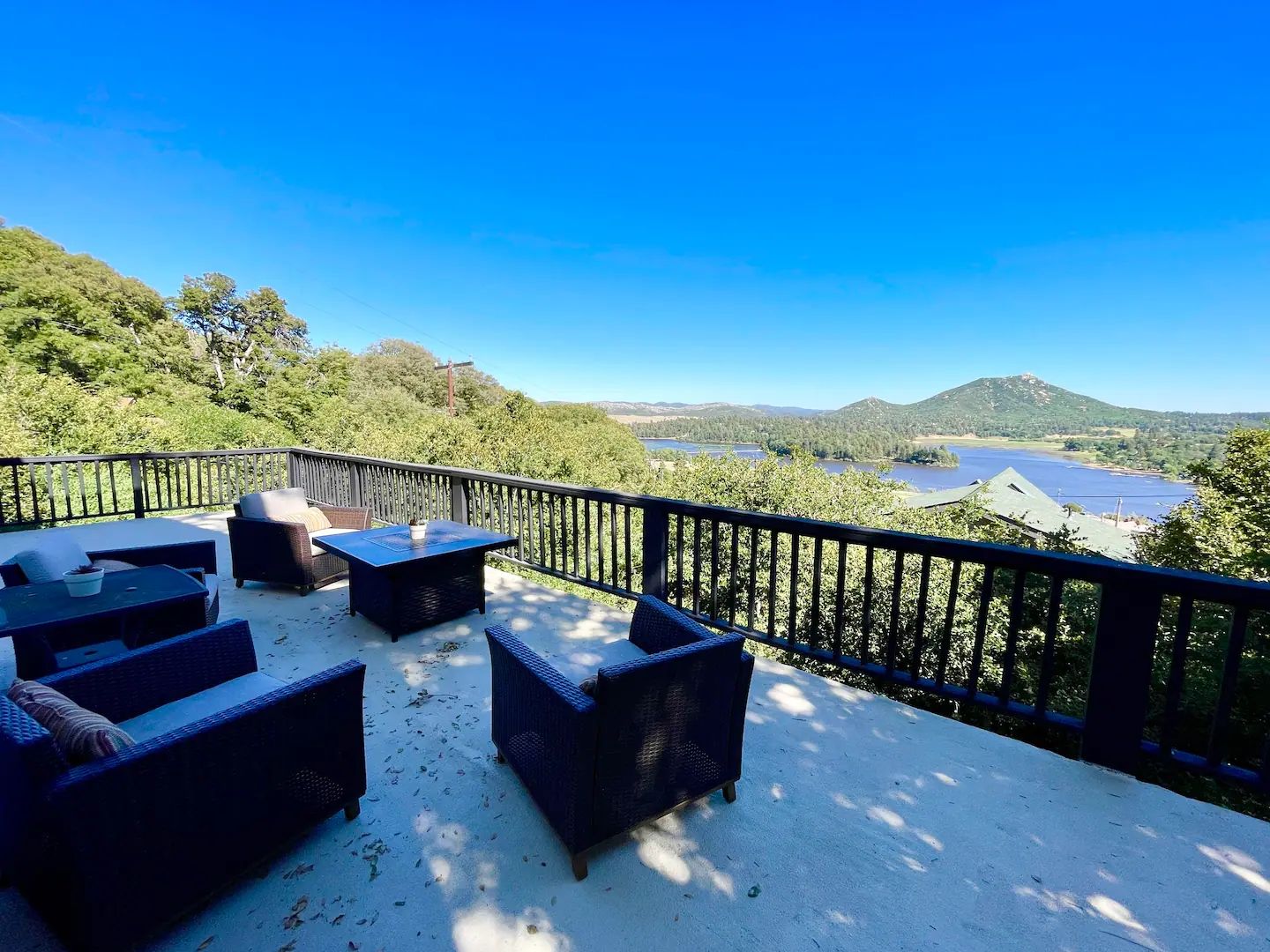 A deck with outdoor furniture overlooking a lake and hills.