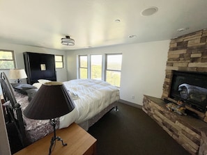 Un dormitorio con cama, mesita de noche, lámpara, cómoda, chimenea y un ventanal grande.