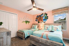 A bedroom with two beds, a ceiling fan, a window with blinds, and a wall with a tropical mural. - 9 Bedroom Villa With Pool at Storey Lake (Kissimmee)