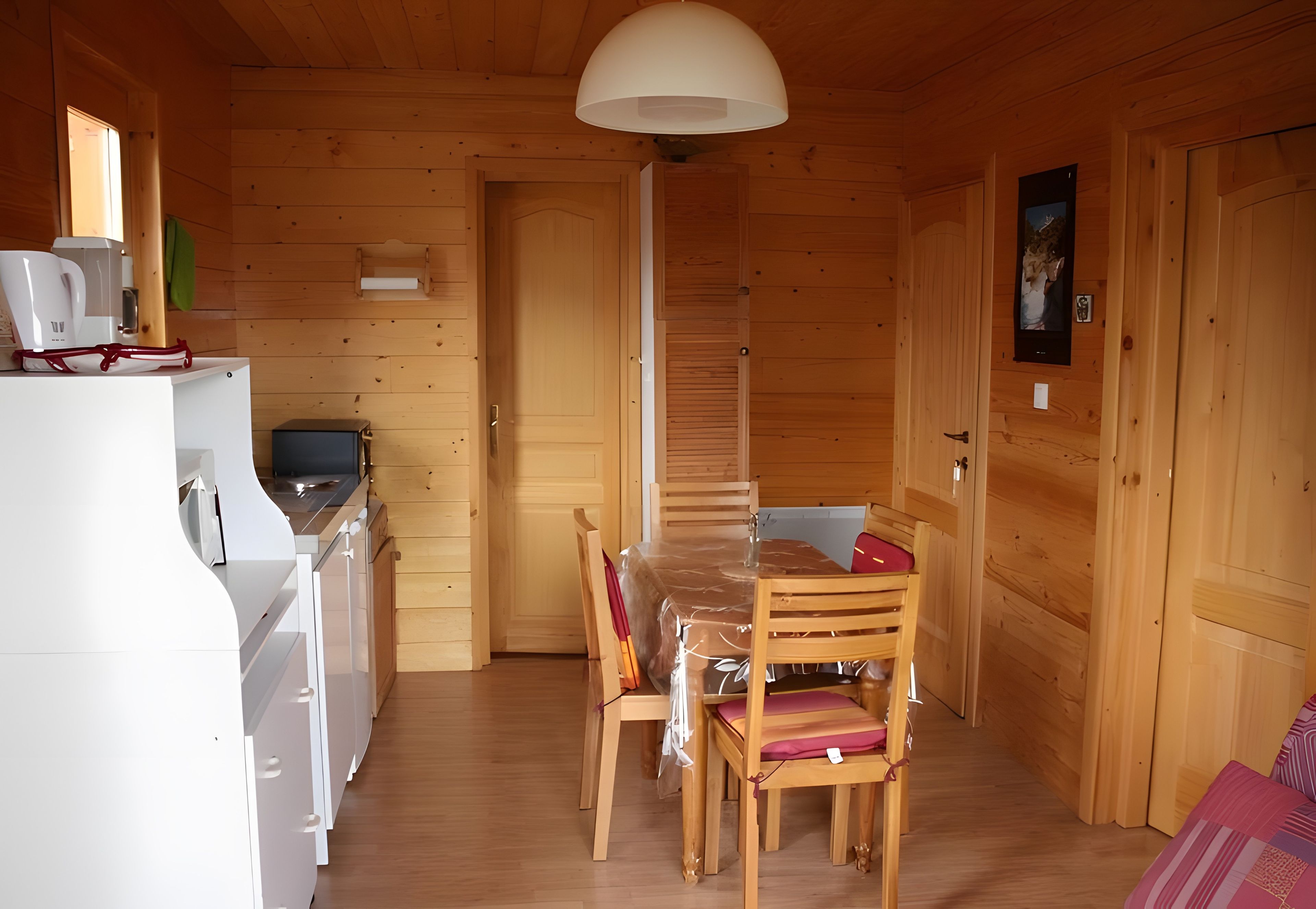A wooden interior with a dining table, chairs, a white refrigerator, a coffee maker, and a television.