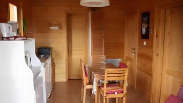 A wooden interior with a dining table, chairs, a white refrigerator, a coffee maker, and a television.