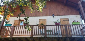 A wooden balcony with potted plants and a view of a building with wooden shutters. - Apartment 'Gîte 2 Personnes, En Montagne' with Mountain View and Balcony (Saint-André-d'Embrun)