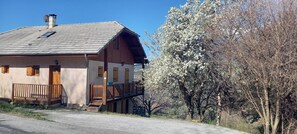 A two-story wooden house with a sloped roof, a balcony, and a small porch. - Apartment 'Gîte 2 Personnes, En Montagne' with Mountain View and Balcony (Saint-André-d'Embrun)