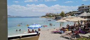 A beach with people swimming and sunbathing, umbrellas, and a hotel in the background. - Family Apartment 150 meters from the beach (Selinia)