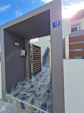 A modern building entrance with a stone-tiled pathway leading to a gated area. - Family Apartment 150 meters from the beach (Selinia)