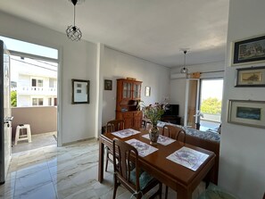 Ein Essbereich mit einem Holztisch, Stühlen und einer Blumenvase. Im Raum befindet sich ein Schrank und ein Fernseher.