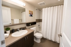 A modern bathroom with a double sink vanity, a toilet, a shower with a curtain, and a mirror above the vanity. - Downtown Toronto 1-Bedroom Apartment | Motion (Toronto)