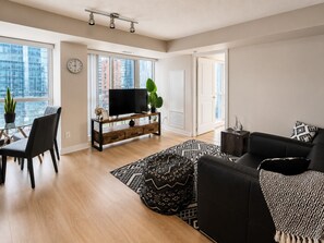 Ein modernes Wohnzimmer mit Flachbildfernseher, einer Couch, einem Essbereich mit Stühlen und einem gemusterten Teppich.
