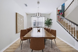 A dining room with a long wooden table, six brown chairs, a chandelier, and a staircase with a railing. - 7BR house sleeps 20 with private pool (Kissimmee)