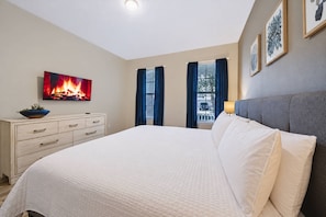 A bedroom with a bed, a dresser, a TV displaying a fireplace, and two windows with curtains. - 7BR house sleeps 20 with private pool (Kissimmee)