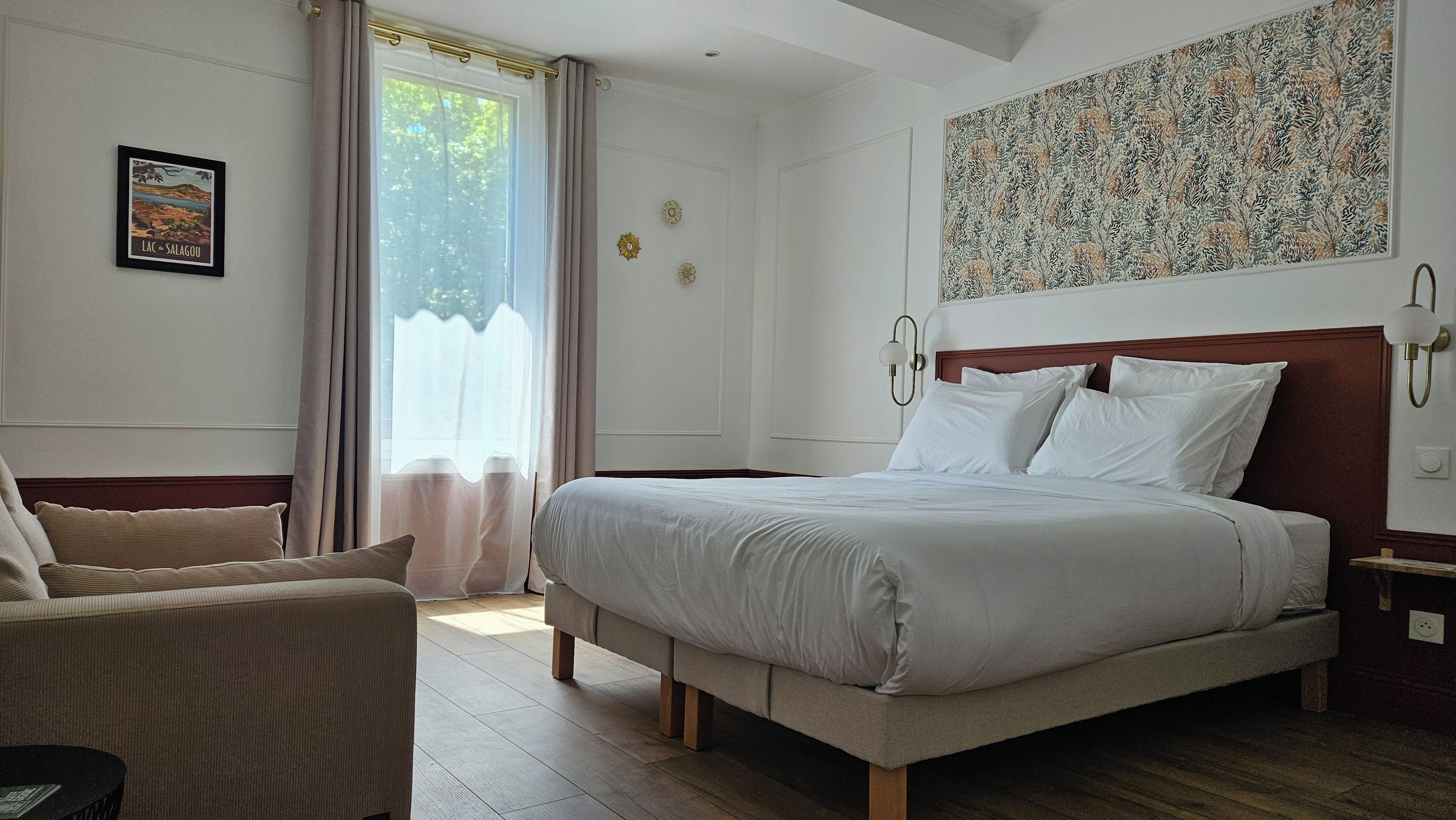 A bedroom with a bed, a chair, a window with curtains, and a wall with a decorative piece.