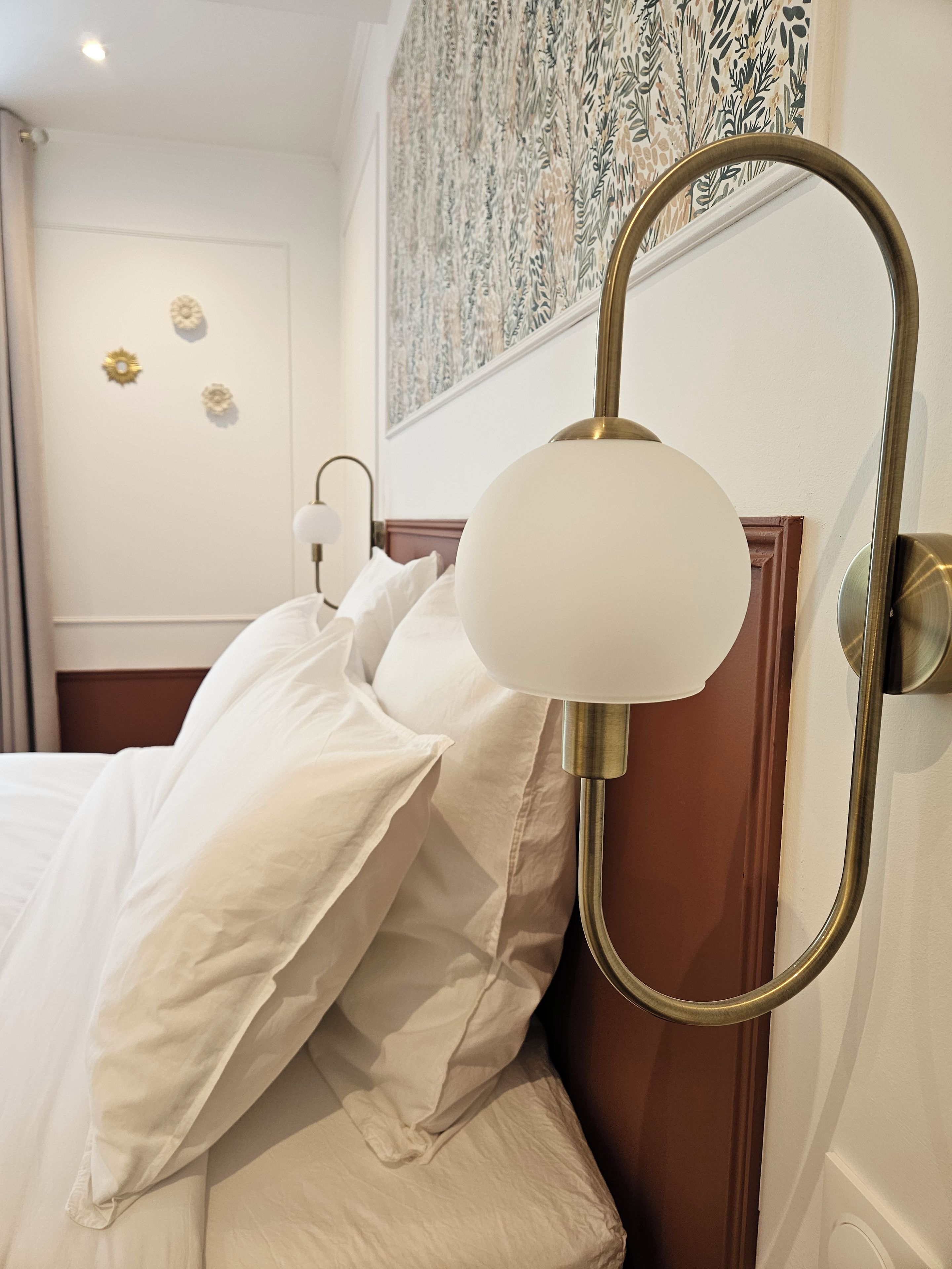 Hotellihuone, jossa on sänky, seinään kiinnitetty valaisin ja koristeellinen seinäelementti.