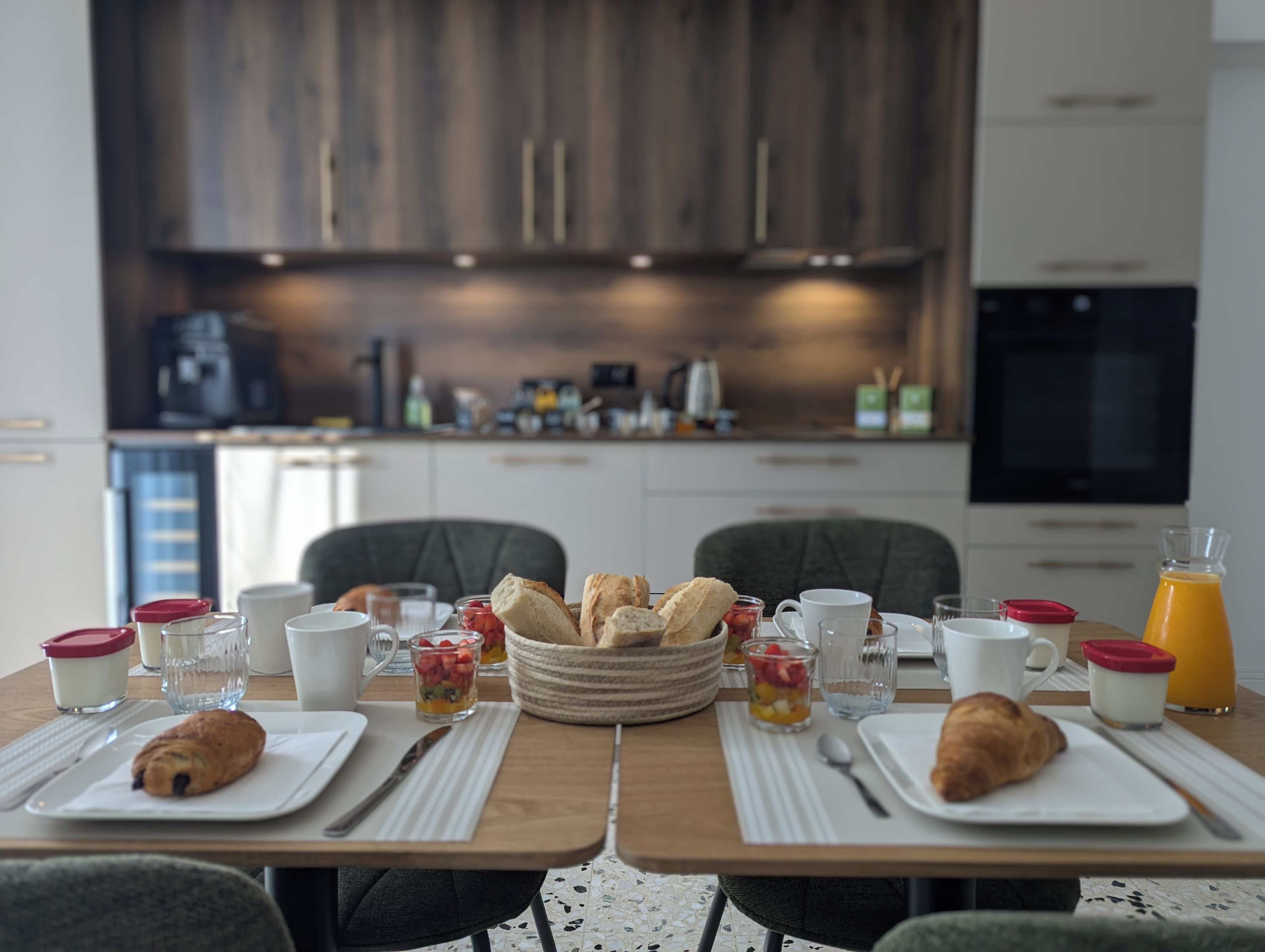 A breakfast setting with a table set for two, featuring croissants, fruit, and beverages.