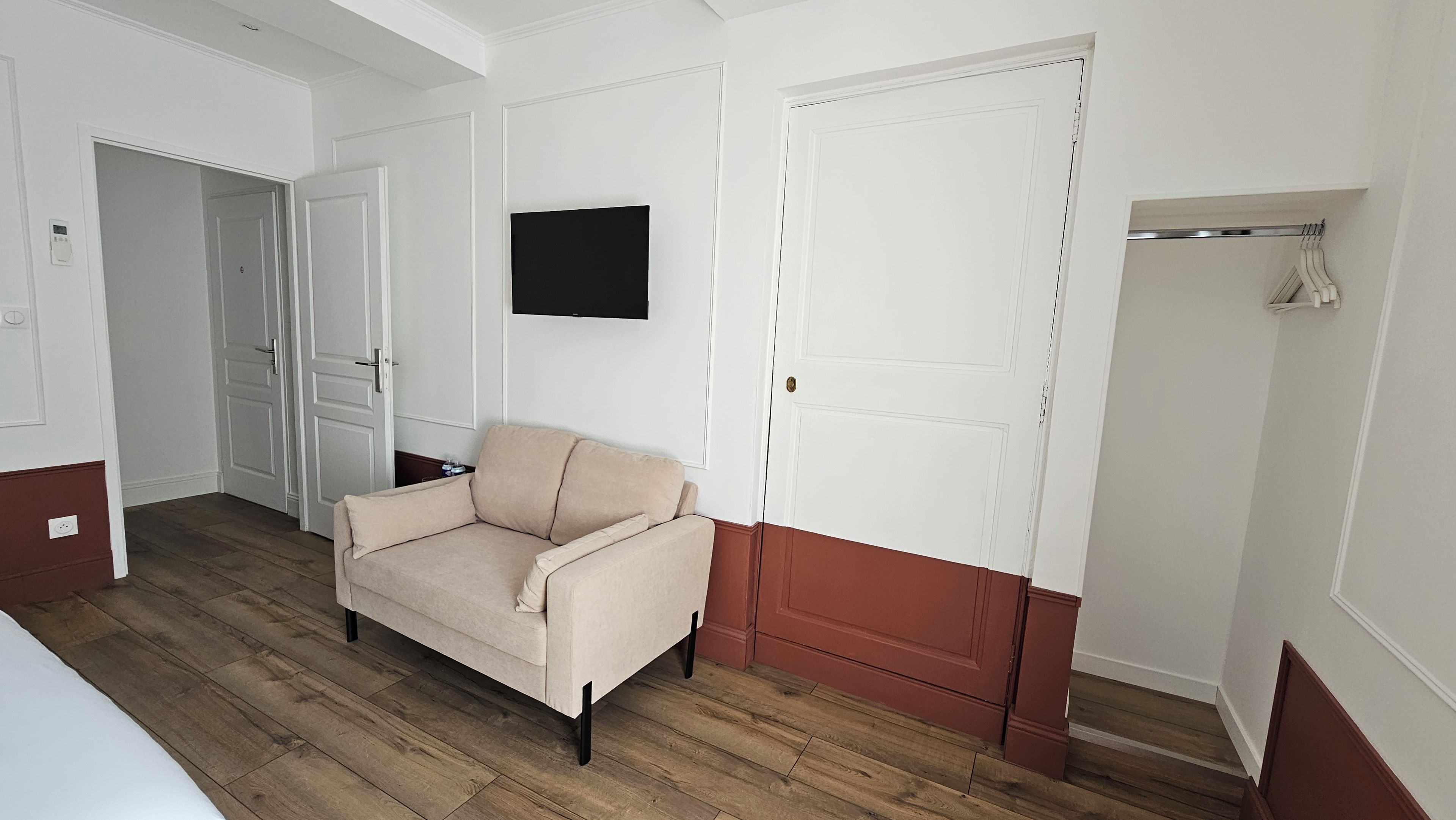 A room with a beige sofa, a flat-screen TV mounted on the wall, and a wooden floor.